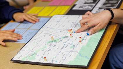 Hands on a table with one of them pointing at a location on a map