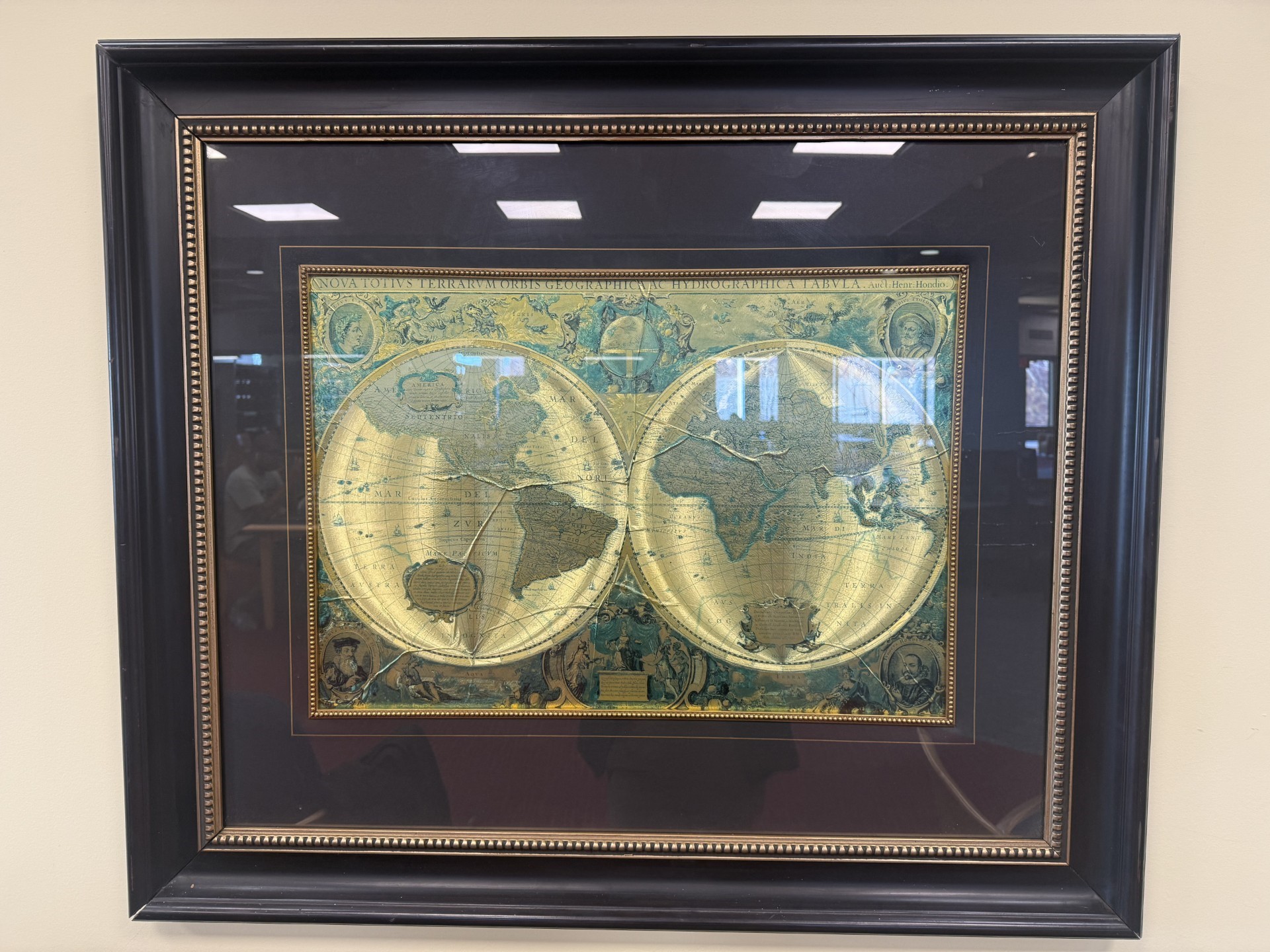 This image shows the new art installation on the wall of the library. Two flat maps of the globe in gold and turquoise, in a dark brown frame.